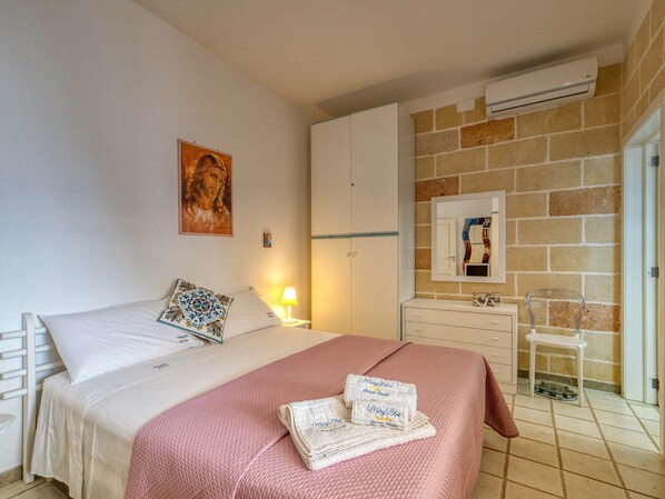 Un dormitorio con cama, mesita de noche, cómoda, espejo y pared de piedra.