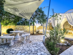 An outdoor patio with stone tables and chairs, a stone wall, and a covered seating area.