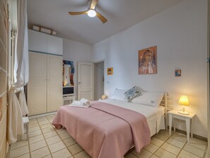A bedroom with a bed, a ceiling fan, a bedside lamp, and a door leading to another room.