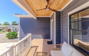 A covered porch with a ceiling fan, a white sofa, and a window with blinds. - Slacktide Bay Retreat - Walk to Beach - Hot Tub, Fire Pit, Gazebo - Sleeps 10 (Lower Township)
