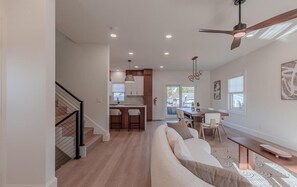 A modern interior with a staircase, a kitchen area, a dining space, and a living room with a sofa and a coffee table. - Slacktide Bay Retreat - Walk to Beach - Hot Tub, Fire Pit, Gazebo - Sleeps 10 (Lower Township)