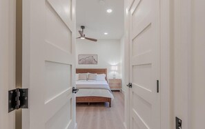 A narrow hallway leading to a bedroom with a bed, bedside table, and a ceiling fan. - Slacktide Bay Retreat - Walk to Beach - Hot Tub, Fire Pit, Gazebo - Sleeps 10 (Lower Township)