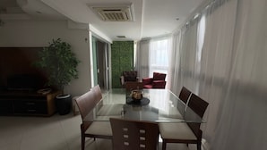 A modern dining area with a glass table, wooden chairs, and a green wall. - Charming 2-bedroom Apartment With Ocean View in Rio (Rio de Janeiro)
