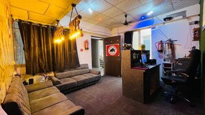 A room with a sofa, a desk with a computer, a chair, and a sign with a warning symbol. - THE BULL GROUP INTERNATIONAL (Surat)