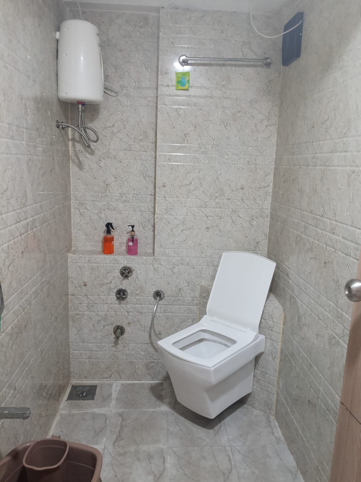 A small, enclosed shower stall with a toilet, a water heater, and a hand soap dispenser.