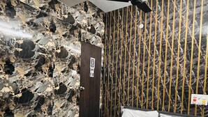 A room with a bed, a ceiling fan, a stone wall, and a door. - THE BULL GROUP INTERNATIONAL (Surat)