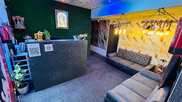 A reception area with a dark reception desk, a cushioned seating area, and a wall with a decorative light fixture. - THE BULL GROUP INTERNATIONAL (Surat)