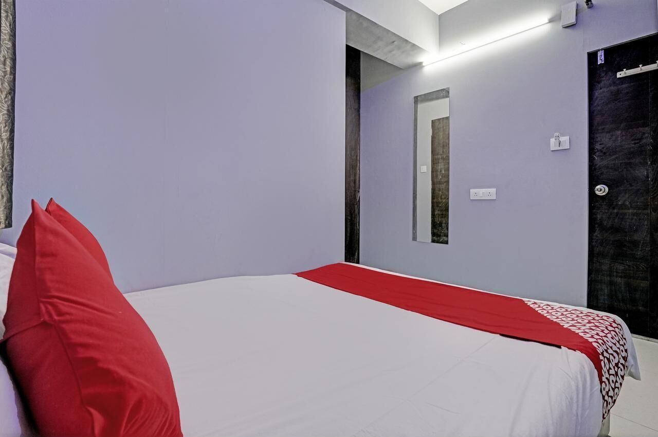 Quarto com cama, travesseiro vermelho, cobre branca, espelho e porta.