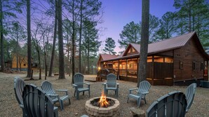 Eine Holzhütte mit Lagerfeuerstelle und Adirondack-Stühlen in einer Waldlandschaft.