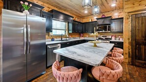 A modern kitchen with a stainless steel refrigerator, a marble island, and pink cushioned stools. - Pretty in Pink: Sleeps 14 (Broken Bow)