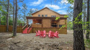A wooden cabin with a porch, a staircase, and red Adirondack chairs. - Pretty in Pink: Sleeps 14 (Broken Bow)