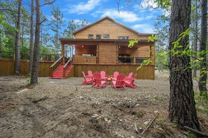 Eine Holzhütte mit Veranda, Treppe und roten Adirondack-Stühlen.