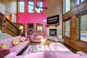 Ein Interieur einer Holzhütte mit rosa Wand, Kamin, Deckenventilator und einem Schild mit der Aufschrift 'Broken Bow Cabin Rentals'.