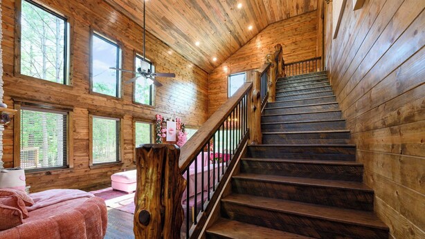 A wooden interior with a staircase, wooden walls, and large windows. - Pretty in Pink: Sleeps 14 (Broken Bow)