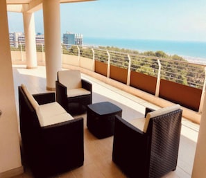 Ein Balkon mit Korbmöbeln und Blick aufs Meer.