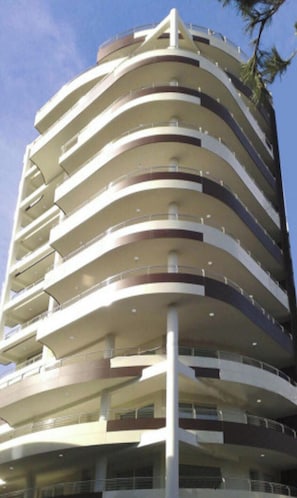 Ein mehrstöckiges Gebäude mit einer geschwungenen Fassade und Balkonen an jeder Etage, sowie einer zentralen, vertikalen Struktur.