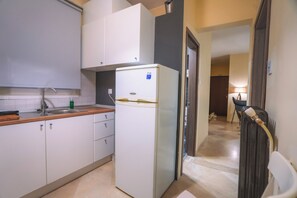 Una cocina compacta con armarios blancos, un fregadero y un refrigerador.