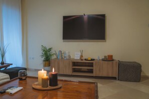 Ein modernes Wohnzimmer mit flachbildfernseher an der Wand, einem Holztisch mit Kerzen, einer Topfpflanze und einer gemütlichen Sitzecke.