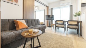 Un salon moderne comprenant un canapé, une table basse et des fauteuils, un téléviseur à écran plat et une grande fenêtre.