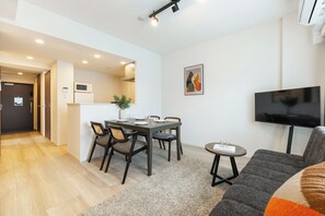 A modern living room with a sofa, a TV, a dining area with a table and chairs, and a kitchen in the background. - Dash Living Ryogoku East  (Tokyo)