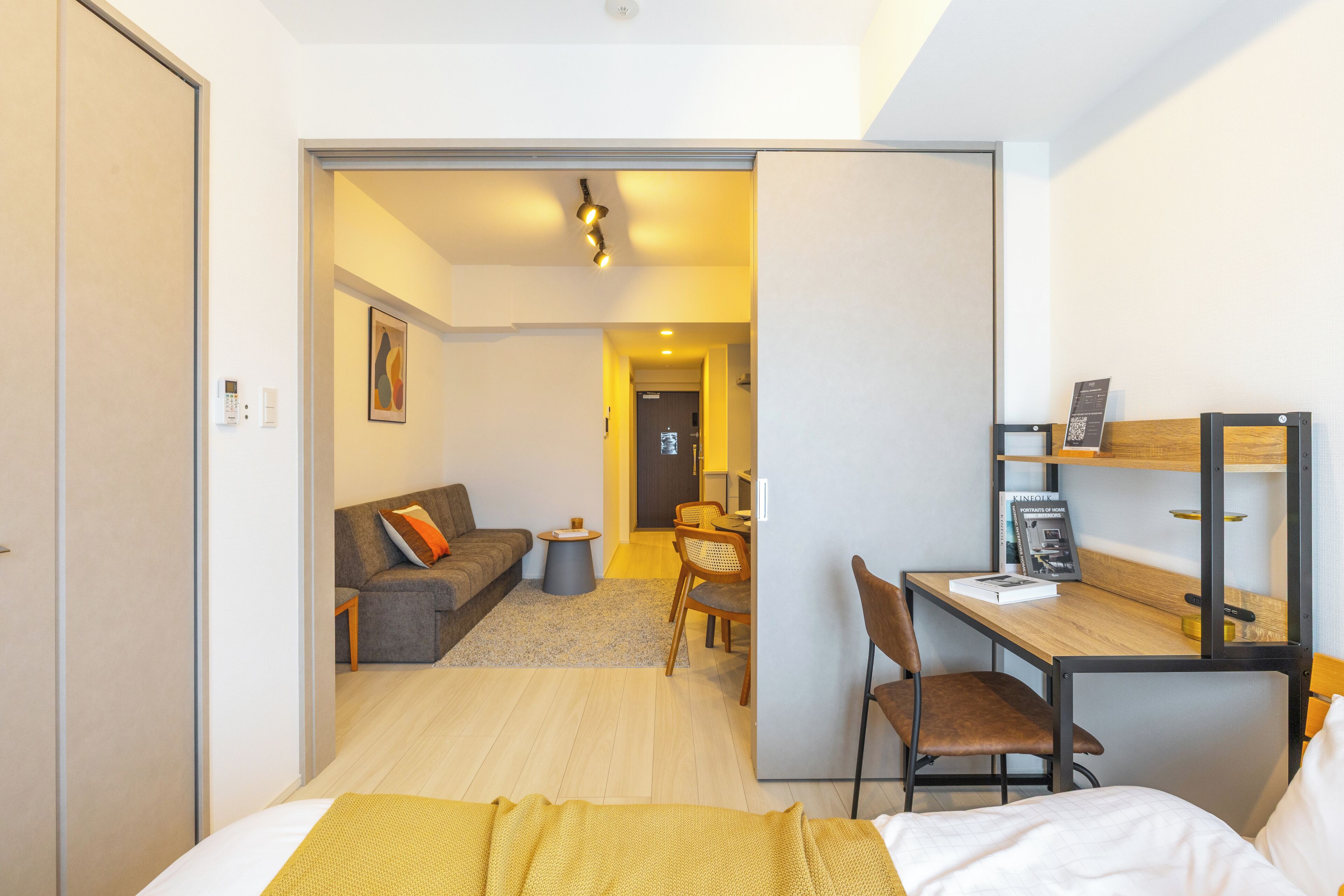 A hotel room with a bed, a desk, a chair, a sofa, a small table, and a door leading to another room.