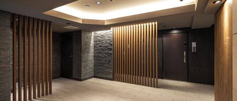 A modern interior with a recessed ceiling, wooden slats, stone walls, and a tiled floor.