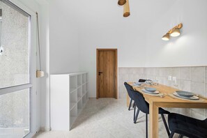 Un coin repas avec une table en bois dressée pour deux personnes, une étagère blanche et une porte en bois.