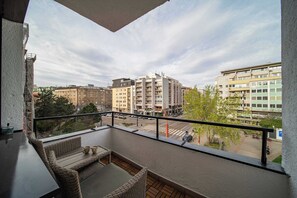 En balkon med fletmøbler, udsigt over et bybillede med bygninger, og en klar himmel.