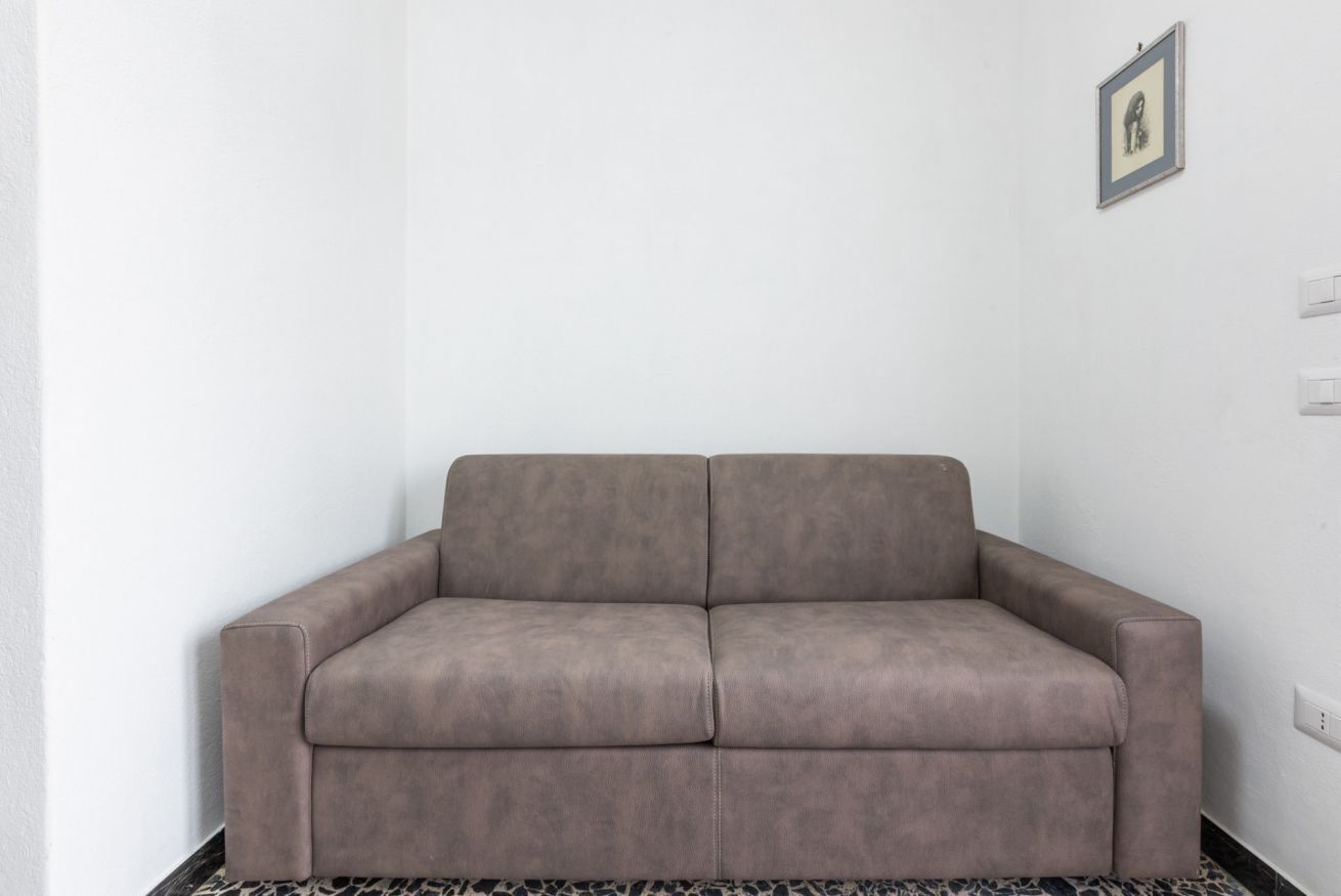 A grey sofa in a room with white walls and a framed picture on the wall.