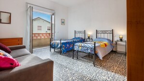 A bedroom with two beds, a sofa, a wooden door, and a patterned floor. - A cozy and spacious 80 square meters apartment, perfect for four people, located on the first floor of a typical Sant'Antioco building (NO elevator).The property is located a short distance from the town center and offers quick access to the seafront. It (Sant'Antioco)