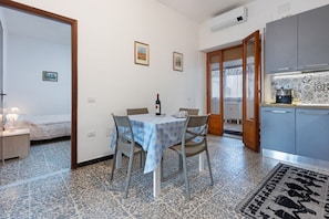 A room with a dining table, chairs, a bed, a kitchenette, and a patterned floor.