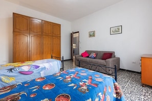 A bedroom with two beds, a wardrobe, a sofa, and a mirror.