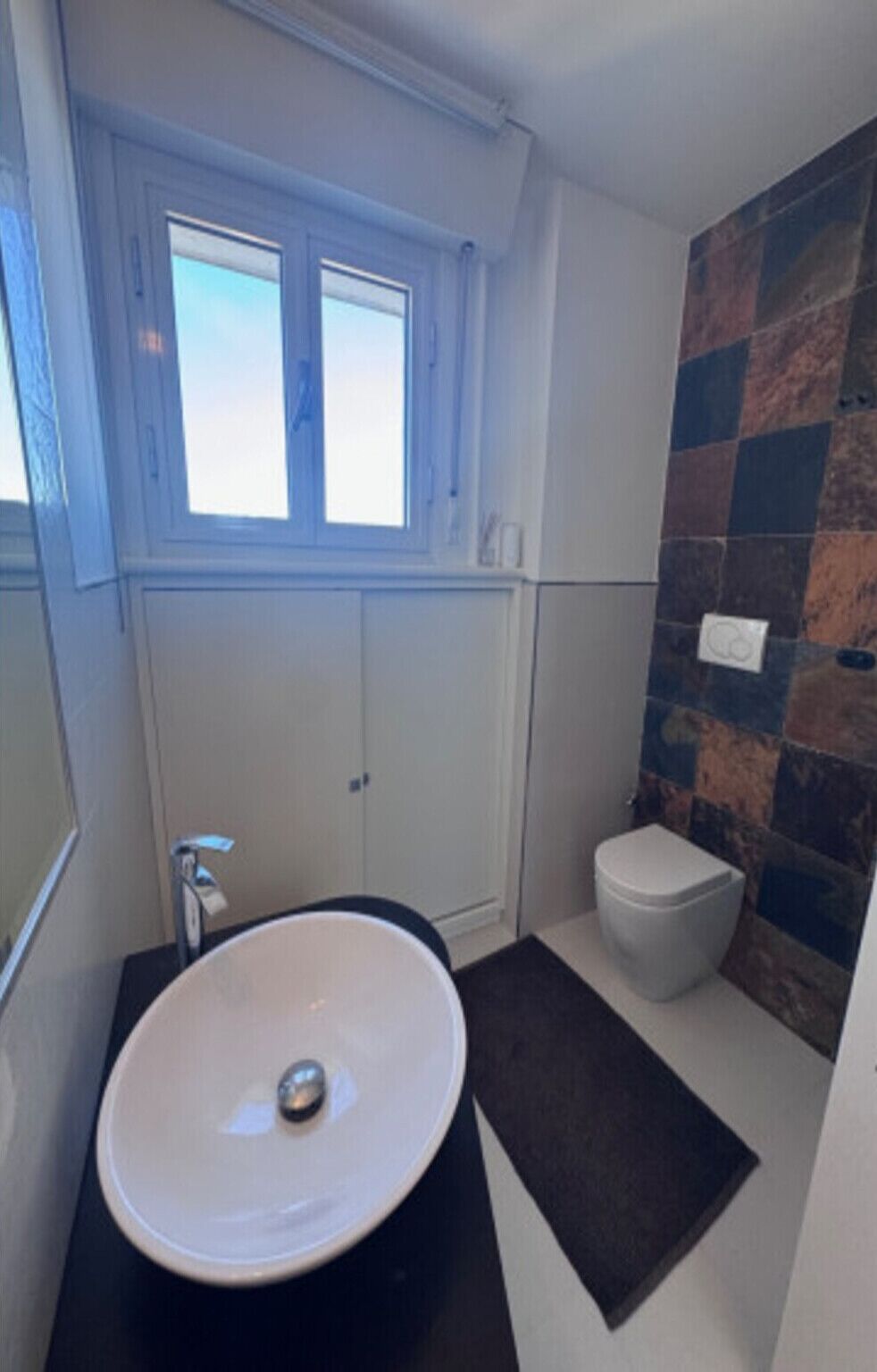 A bathroom with a white sink, a toilet, and a window above the sink.