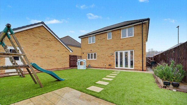 A residential property with a brick house, a wooden deck, a green lawn, and a play area with a slide.