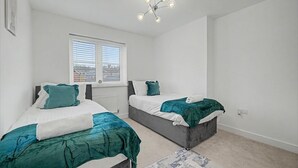 A bedroom with two beds, a window, a ceiling light fixture, and a radiator.