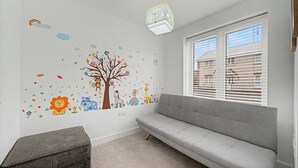 A child's room with a grey sofa, a small ottoman, and a wall decorated with a tree and animal decals.