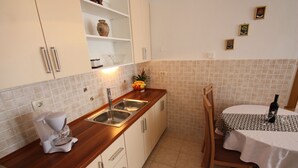 A kitchen with a wooden countertop, white cabinets, a coffee maker, a fruit bowl, a sink, and a dining table with a wine bottle. - Apartment for 4 with sea view, balcony and parking in Jadranovo (Jadranovo)