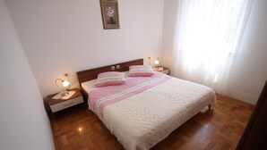 A bedroom with a wooden floor, a bed with a white quilt, two bedside lamps, and a nightstand with a lamp. - Apartment for 4 with sea view, balcony and parking in Jadranovo (Jadranovo)
