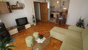 A living room with a sofa, ottoman, television, and a small table with a plant. - Apartment for 4 with sea view, balcony and parking in Jadranovo (Jadranovo)