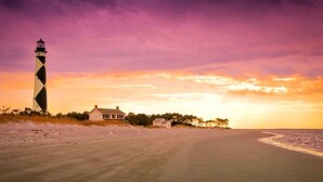 A lighthouse, a beach, and a house by the sea during sunset. - Beautiful 3BR Condo in OBX, NC, Beach, Pools, Hot Tub, Family Resort Aug. 9-15 (duck)