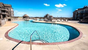 A swimming pool with a wooden deck, lounge chairs, and a view of the surrounding buildings. - Beautiful 3BR Condo in OBX, NC, Beach, Pools, Hot Tub, Family Resort Aug. 9-15 (duck)