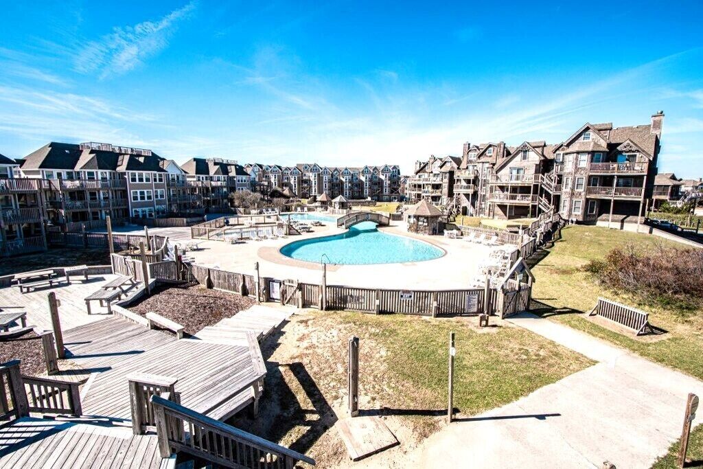 A pool area surrounded by wooden deck and buildings with balconies.