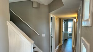 A hallway with a wooden staircase, a light switch, and a door leading to another room. - Beautiful 3BR Condo in OBX, NC, Beach, Pools, Hot Tub, Family Resort Aug. 9-15 (duck)