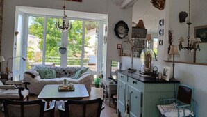 Un salon chaleureux avec un canapé, une table à manger, des chaises et un coin cuisine doté de placards et d’un lustre suspendu.