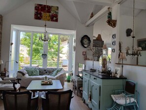 A cozy living room with a sofa, dining table, chairs, and a kitchen area with cabinets and a hanging chandelier. - Chat Fleurs" family home Pornichet center very quiet (Pornichet)