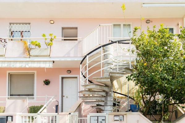 Un edificio de varios pisos con una escalera espiral, balcones con plantas y una puerta.