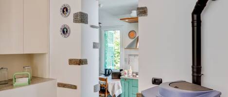 A kitchen with a sink, a window with shutters, and a door leading to another room.