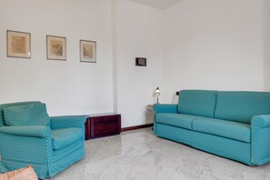 Ein Wohnzimmer mit zwei sesseln in Türkis mit Muster, einer kleinen Holzkommode und drei gerahmten Kunstwerken an der Wand.