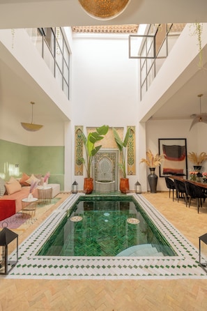 A spacious indoor area with a central glass pool, a high ceiling, and a seating area with a sofa and chairs. - Riad Dar Fiji - Elegant Exclusive Riad with Private Pool & Rooftop Jacuzzi (Marrakesh)