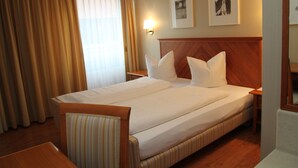 A hotel room with a large bed, a wooden headboard, a bedside table, a chair, and a window with curtains.